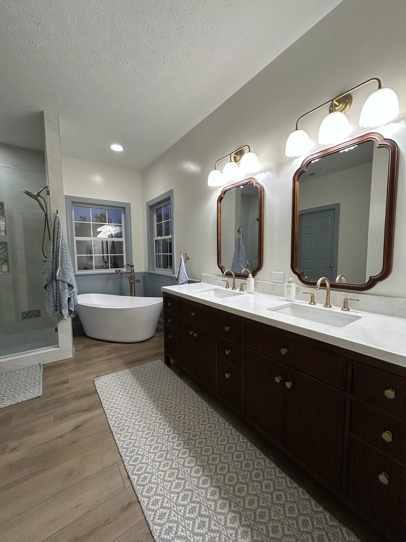 Remodeled bathroom with a double vanity, dark wood cabinets, brass fixtures and a freestanding tub